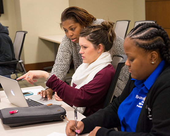 Professor helping a student at a laptop, with another student beside her