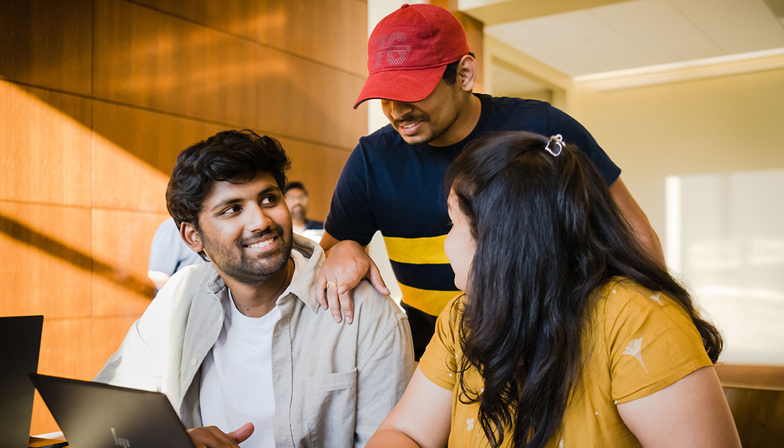 Three students working together while looking at a laptop