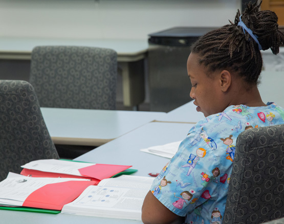 Webster nursing student wearing scrubs studying textbook and notes.